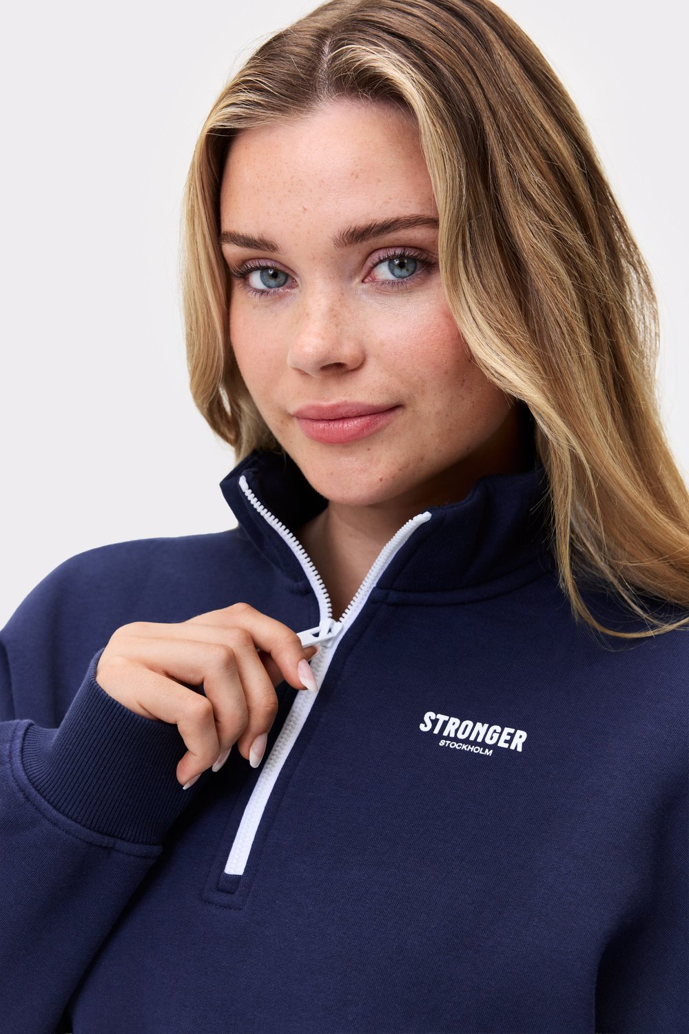 Nahaufnahme eines Models im dunkelblauen Half Zip Sweatshirt von Stronger mit hohem Kragen und weißem Reißverschluss.