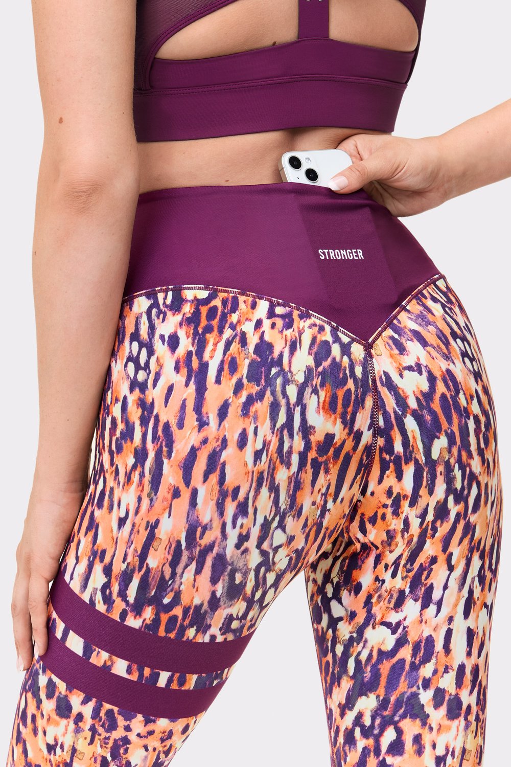 Model putting her phone in the hidden back pocket of the Stronger The Signature One Leggings in Malibu Milk Print.