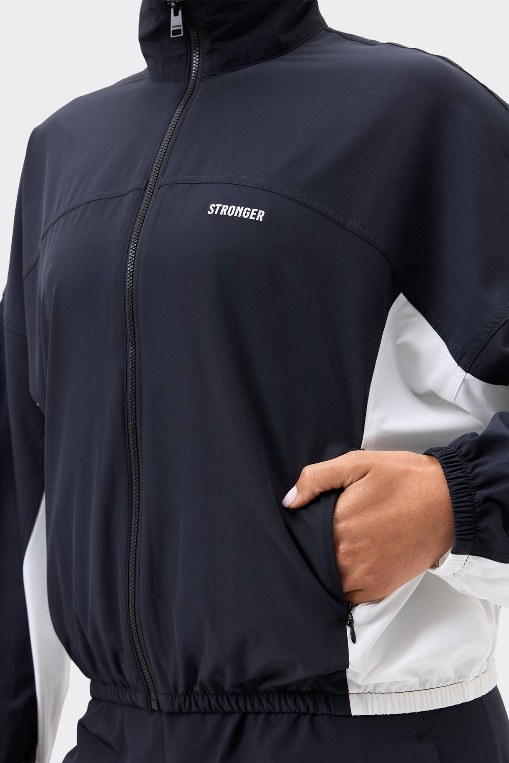 Close-up of Stronger's black and white Breezy Woven Jacket, showing the white chest logo and functional side pocket.