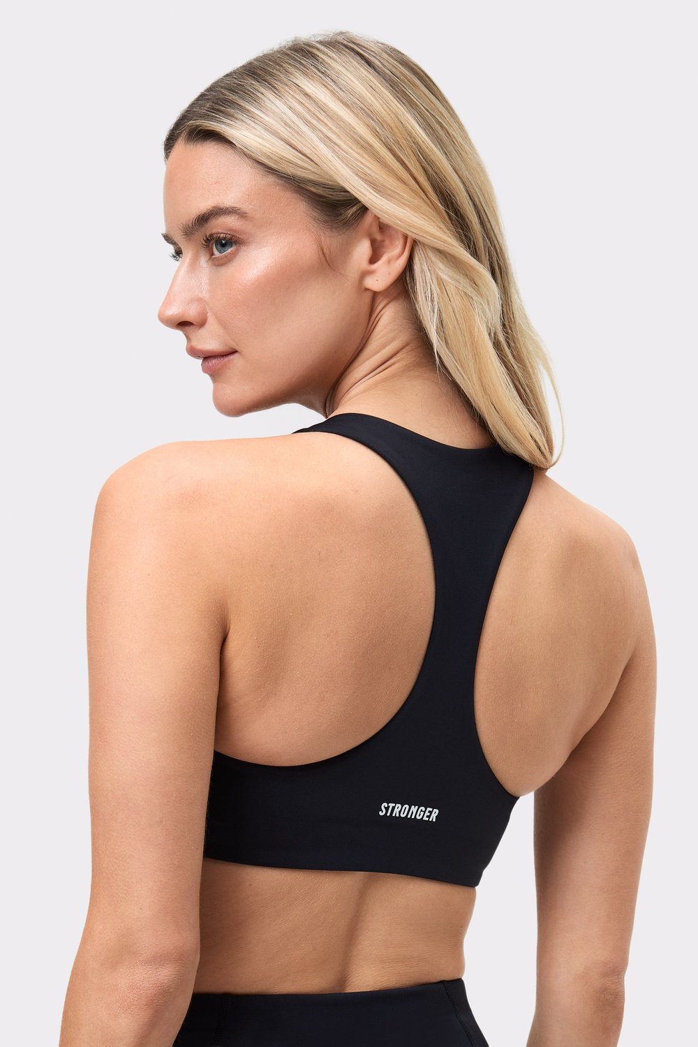 Achteraanzicht van een vrouw in de zwarte Front Closure Sports Bra, met het racerback-ontwerp en het Stronger-logo.