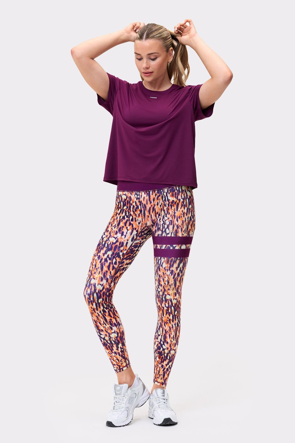 Front view of a model wearing the `Relaxed Tee` in `Aubergine Purple` from `stronger`, paired with patterned leggings.