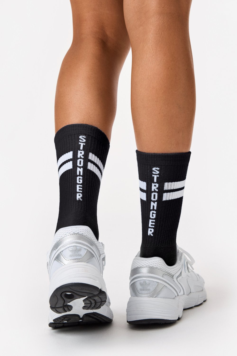 Rückansicht schwarzer gerippter Stride Socks von Stronger mit weißen Signature Lines und Logotyp sowie weißen Sneakern.