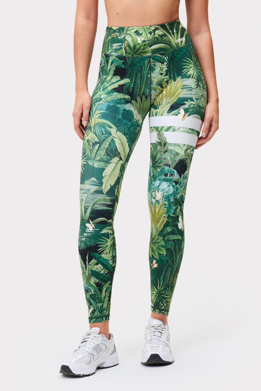 Model in den grünen Explore Printed Leggings mit Tropical Leaves-Print und charakteristischen Streifen von Stronger.