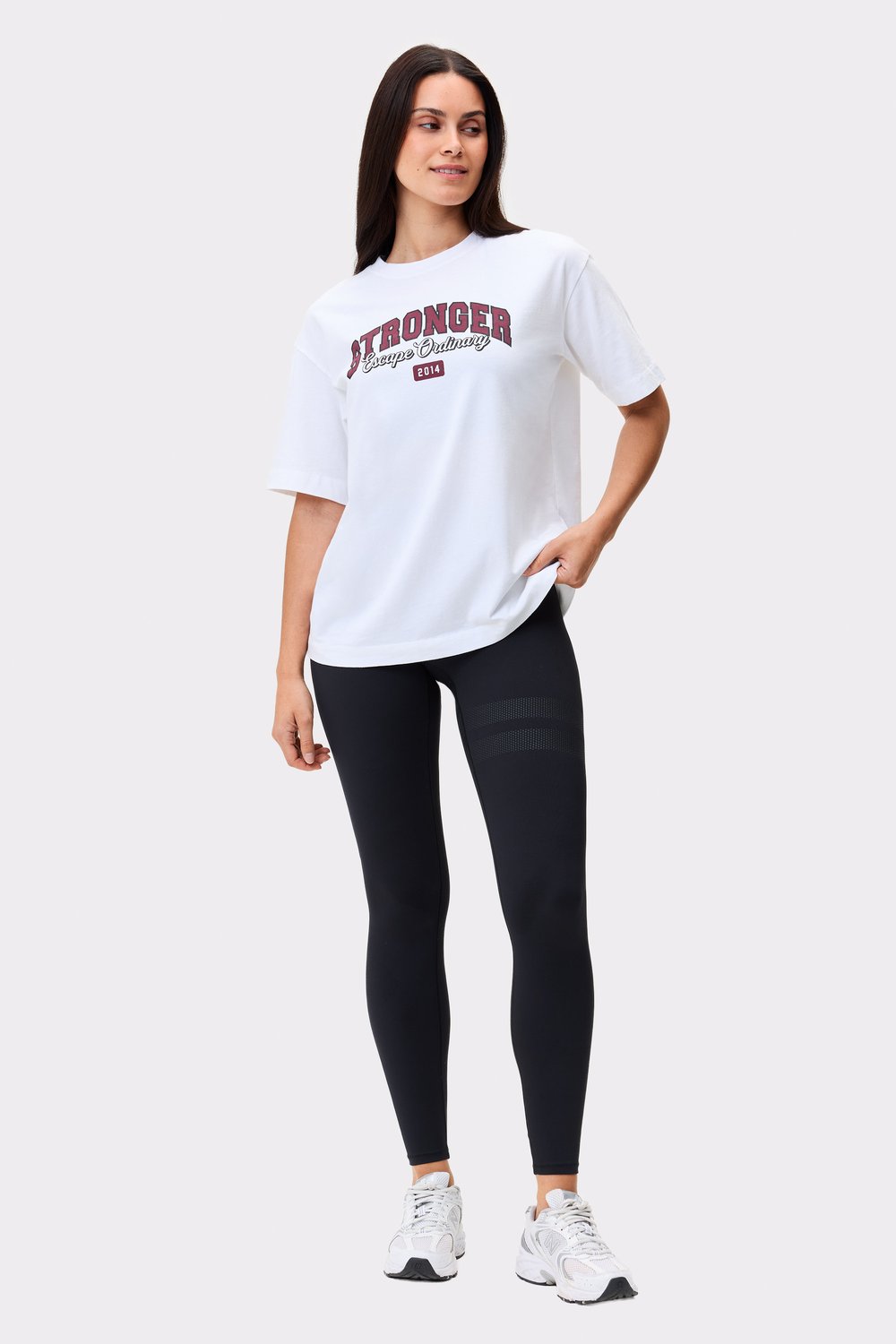 Model trägt das hellweiße Essential T-Shirt von Stronger mit einem Frontprint und schwarzen Leggings.