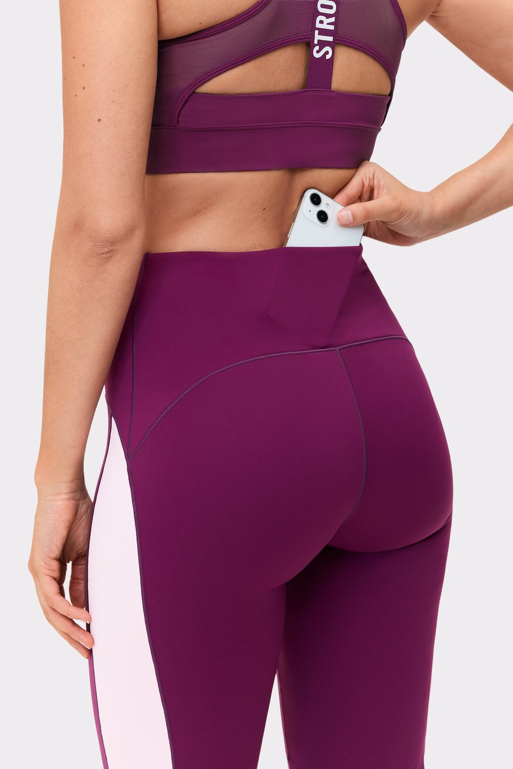Close-up of a model putting her phone in the hidden back pocket of the Stronger Thermal Bootcut Pants in Aubergine Purple.