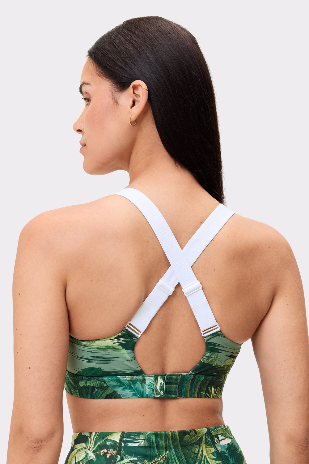 Model trägt den Power Sports Bra von Stronger im Tropical Leaves-Print, mit Fokus auf die Rückseite und verstellbare Träger.