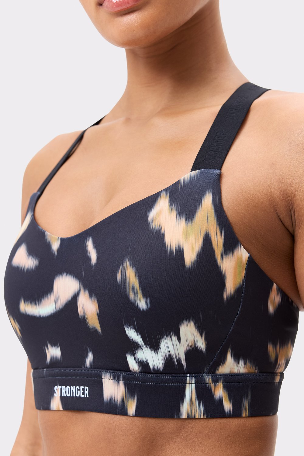 Close-up of Stronger's Power Sports Bra in Savannah Print, featuring a pink abstract pattern and logo-detailed straps.