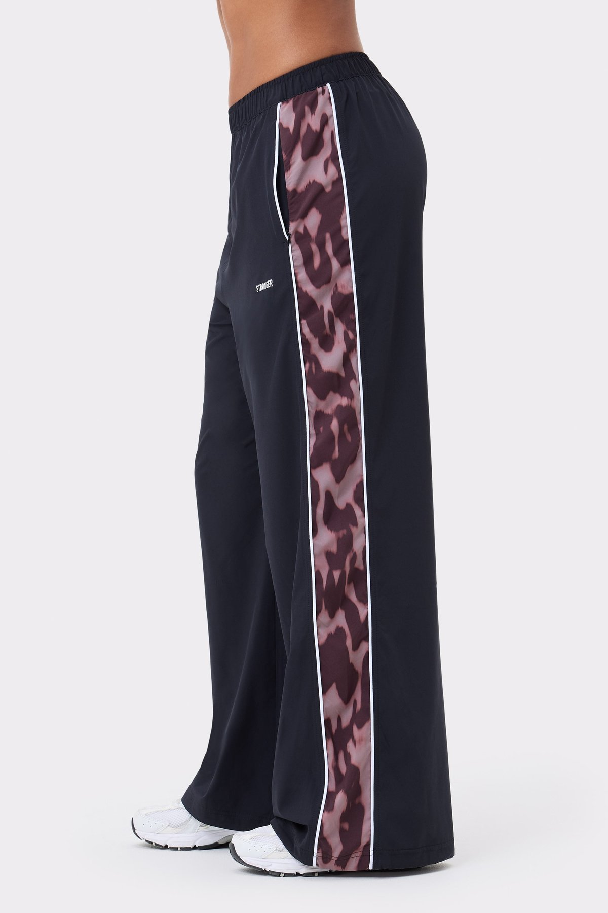 Zijaanzicht van de zwarte Stronger Breezy Woven Pants met roze luipaardprint zijstreep en reflecterend logodetail.