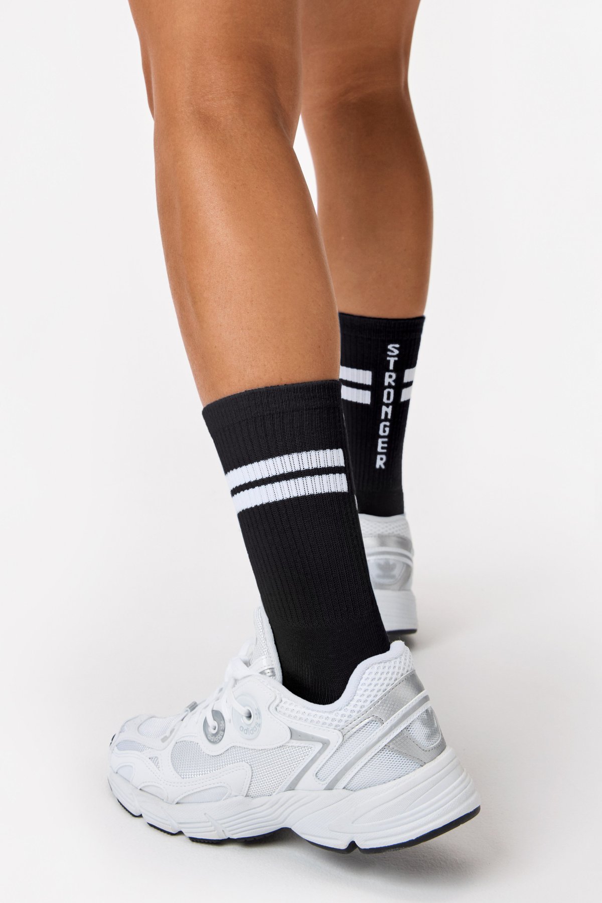 Nahaufnahme: Schwarze Stride Socks von Stronger mit geripptem Stoff, weißen Signature-Streifen und vertikalem Logo.
