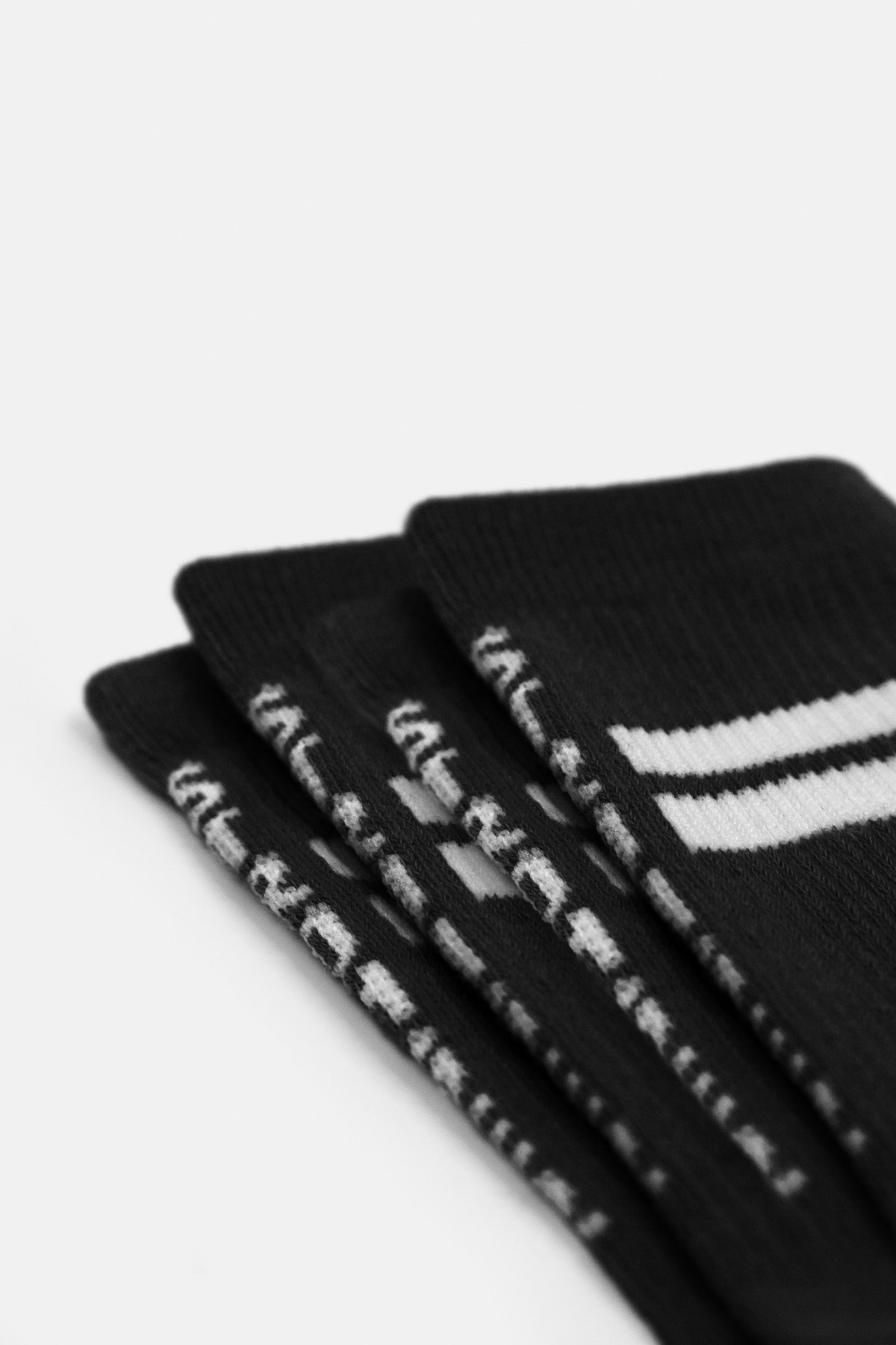 Nahaufnahme der schwarzen Stride Socks 2-pack von Stronger mit weißen Signature Lines und atmungsaktivem Rippstoff.