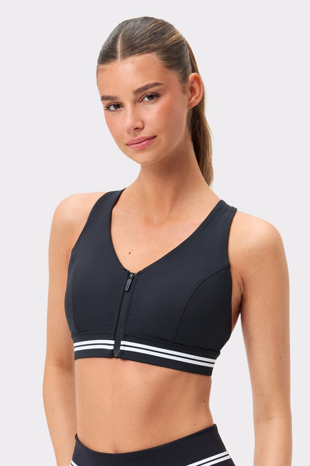 Front view of Stronger's black Signature Logo Zip Sports Bra featuring a front zipper and white striped band.