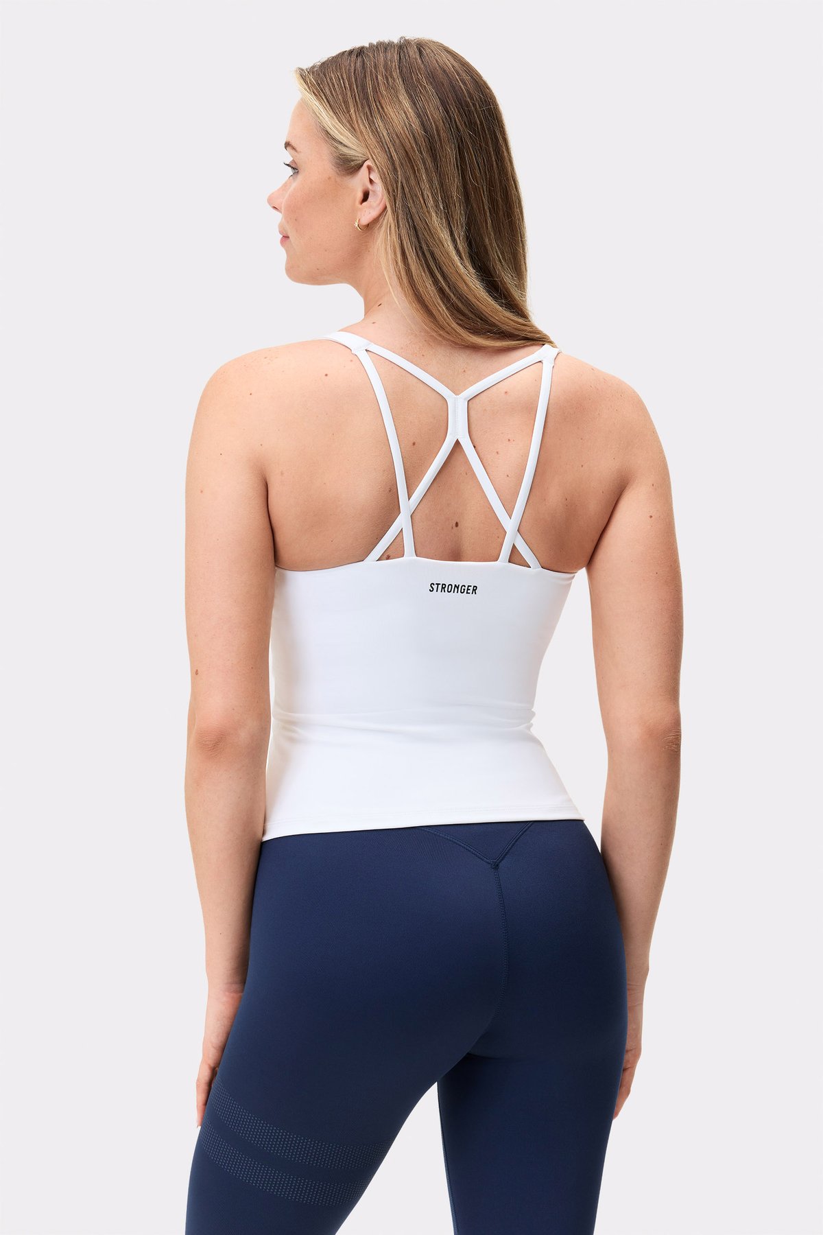 Model im weißen Stronger Signature Strappy Tank, zeigt das schmale Rückendesign mit Trägern und dem Logo.