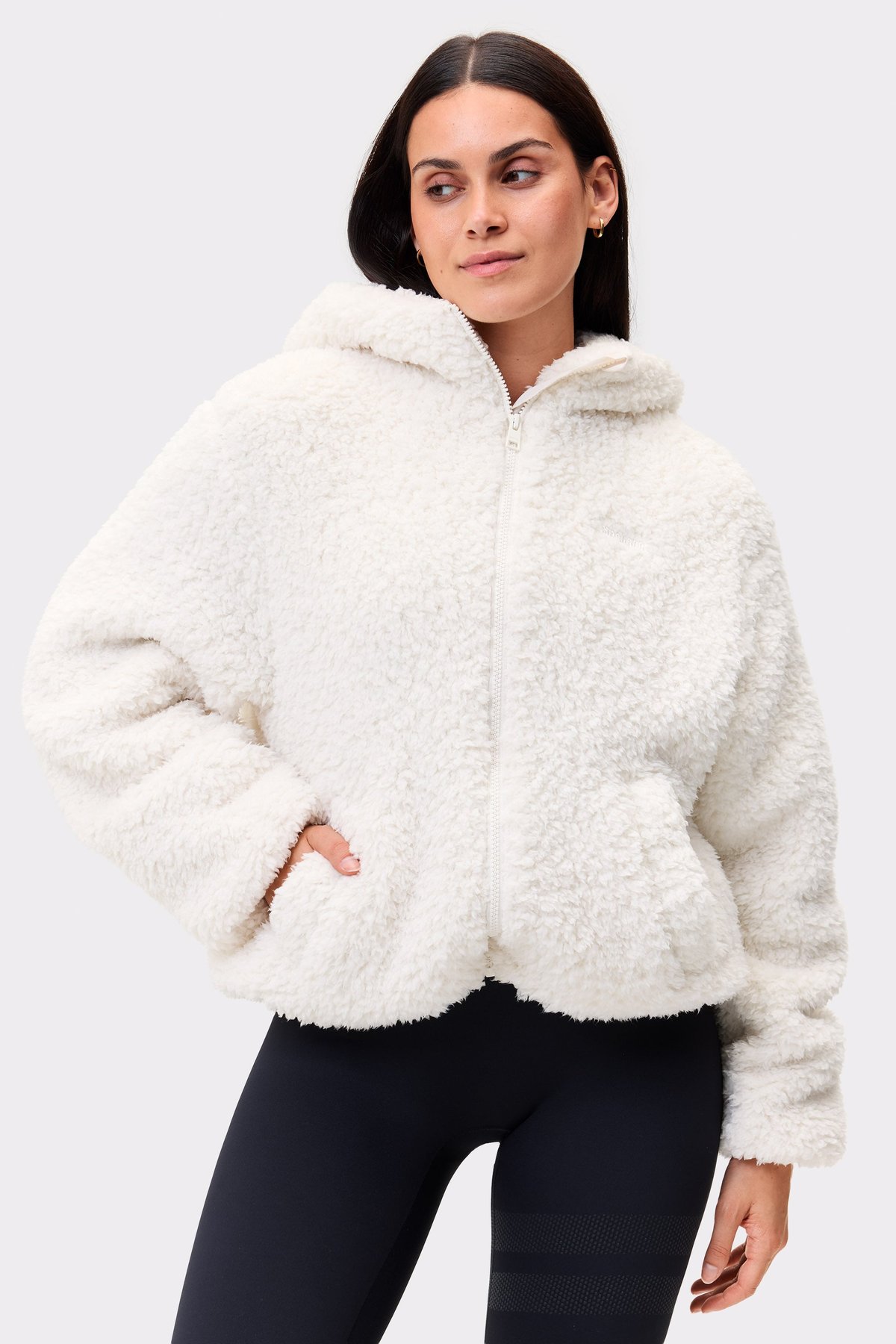 Model trägt weiße Hooded Pile Jacket von Stronger, eine kuschelige Fleece-Jacke mit durchgehendem Reißverschluss und Kapuze.