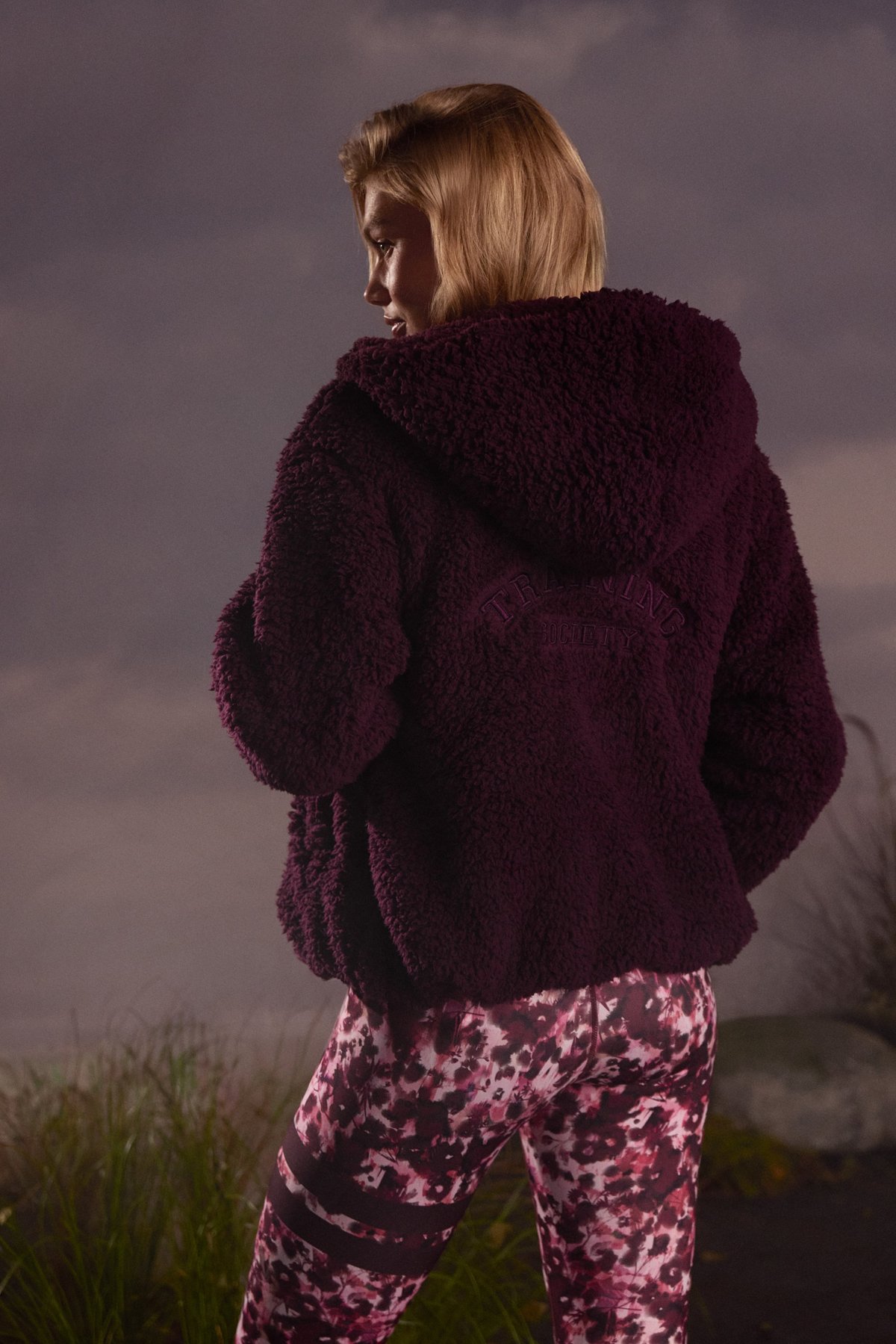 Back view of a woman wearing the dark purple Hooded Pile Jacket from Stronger, showing the soft pile texture.