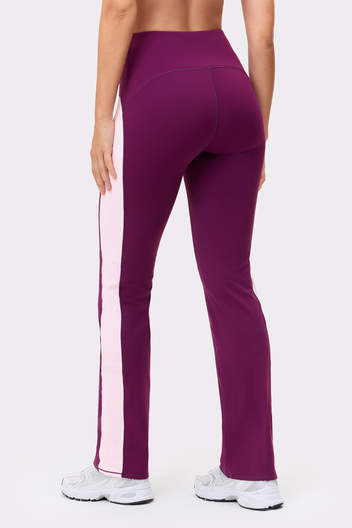 Back view of a model in Stronger Thermal Bootcut Pants in purple, showing pink side panels and flared leg fit.