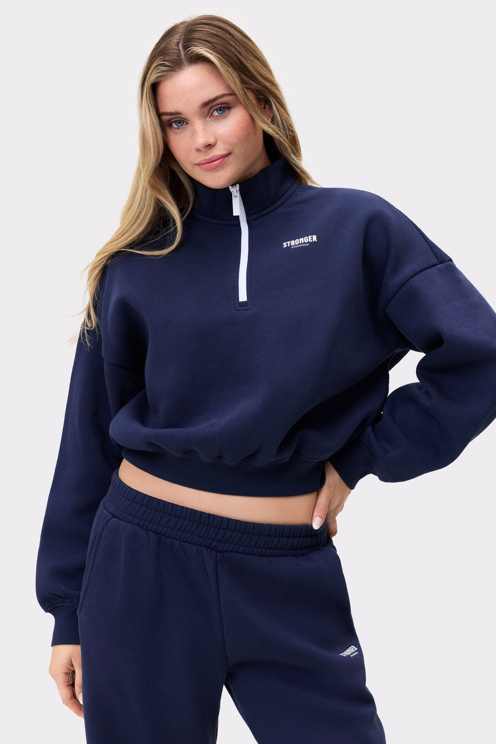 Model trägt das dunkelblaue Half Zip Sweatshirt von Stronger mit verkürzter, lockerer Passform und halbem Reißverschluss.