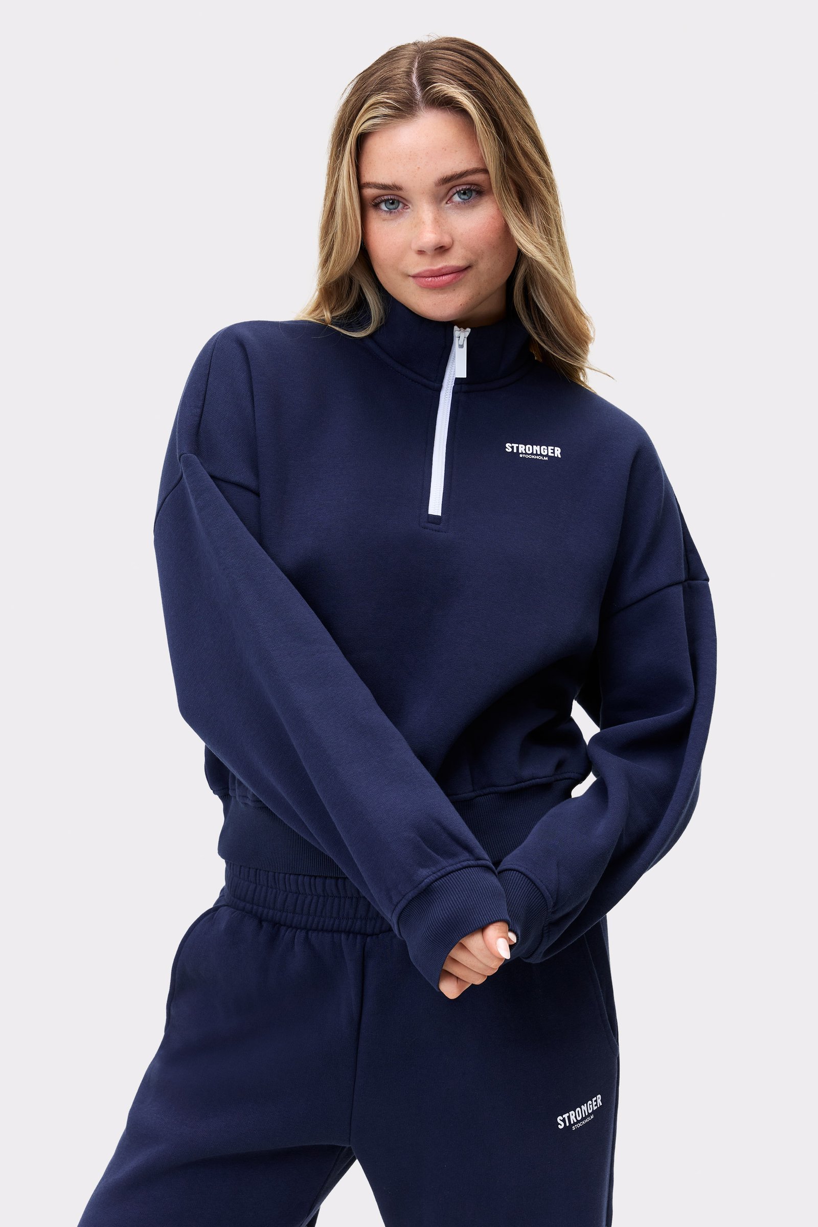 Model in dunkelblauem Half Zip Sweatshirt von Stronger mit halbem Reißverschluss und gedrucktem Logo auf der Brust.