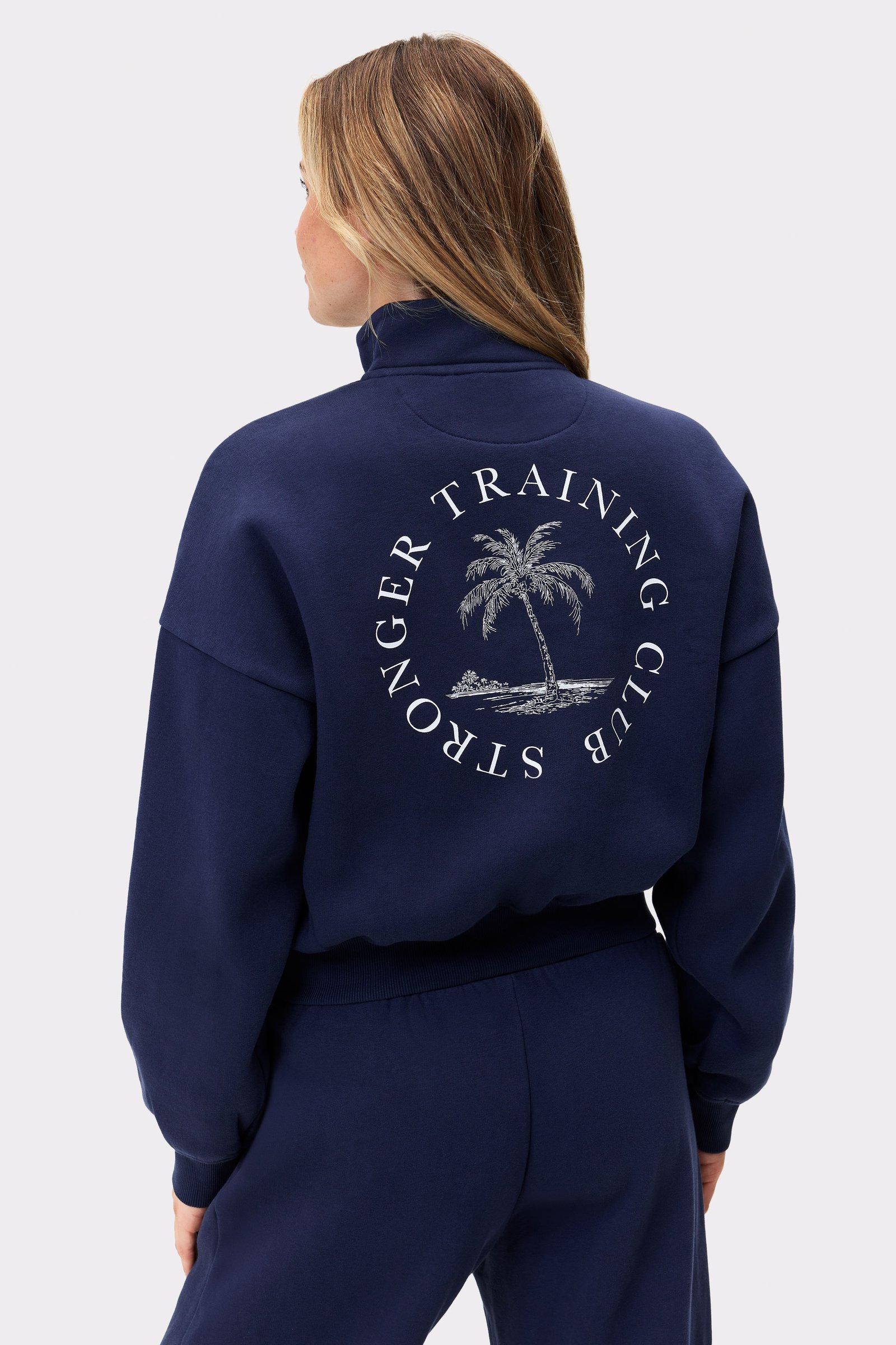 Rückansicht eines Models im dunkelblauen Half Zip Sweatshirt von Stronger mit einem großen runden Grafikprint auf dem Rücken.