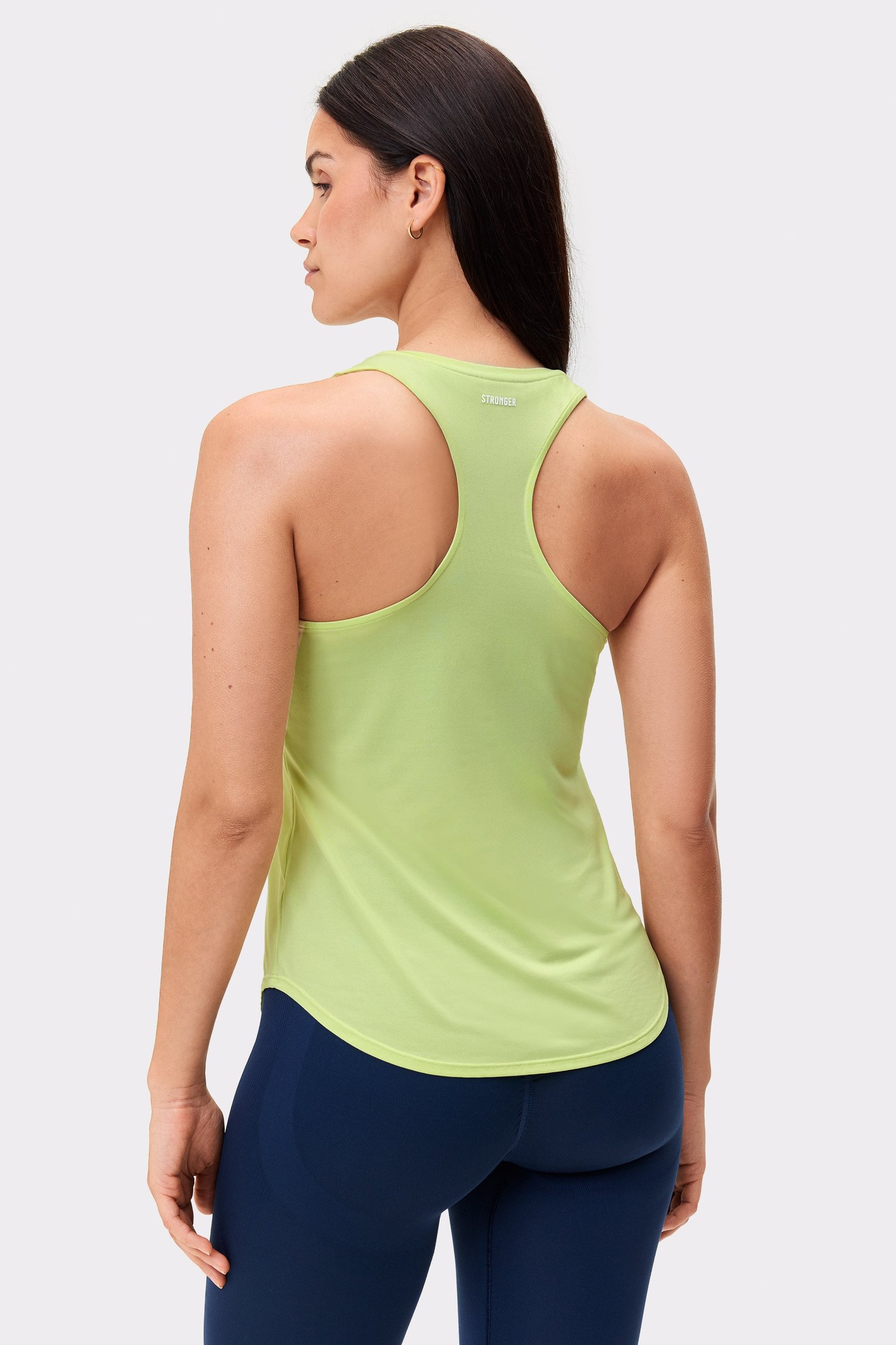 Modell von hinten im limettengrünen Airy Racerback Tank von Stronger, mit Racerback-Design und abgerundetem Saum.