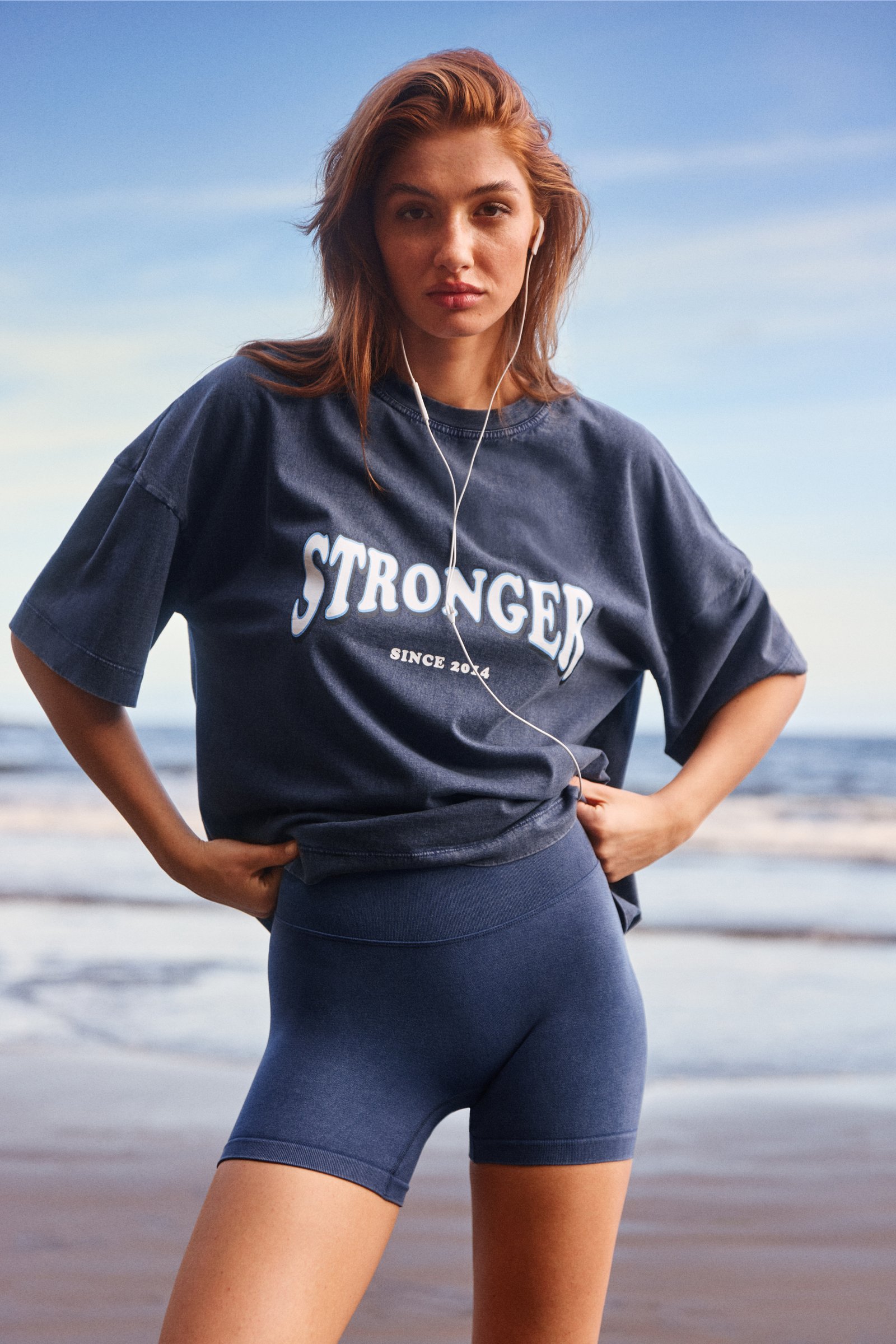 Washed Seamless Shorts met hoge taille in Navy Blazer van Stronger met een gewassen look en logo T-shirt op het strand.