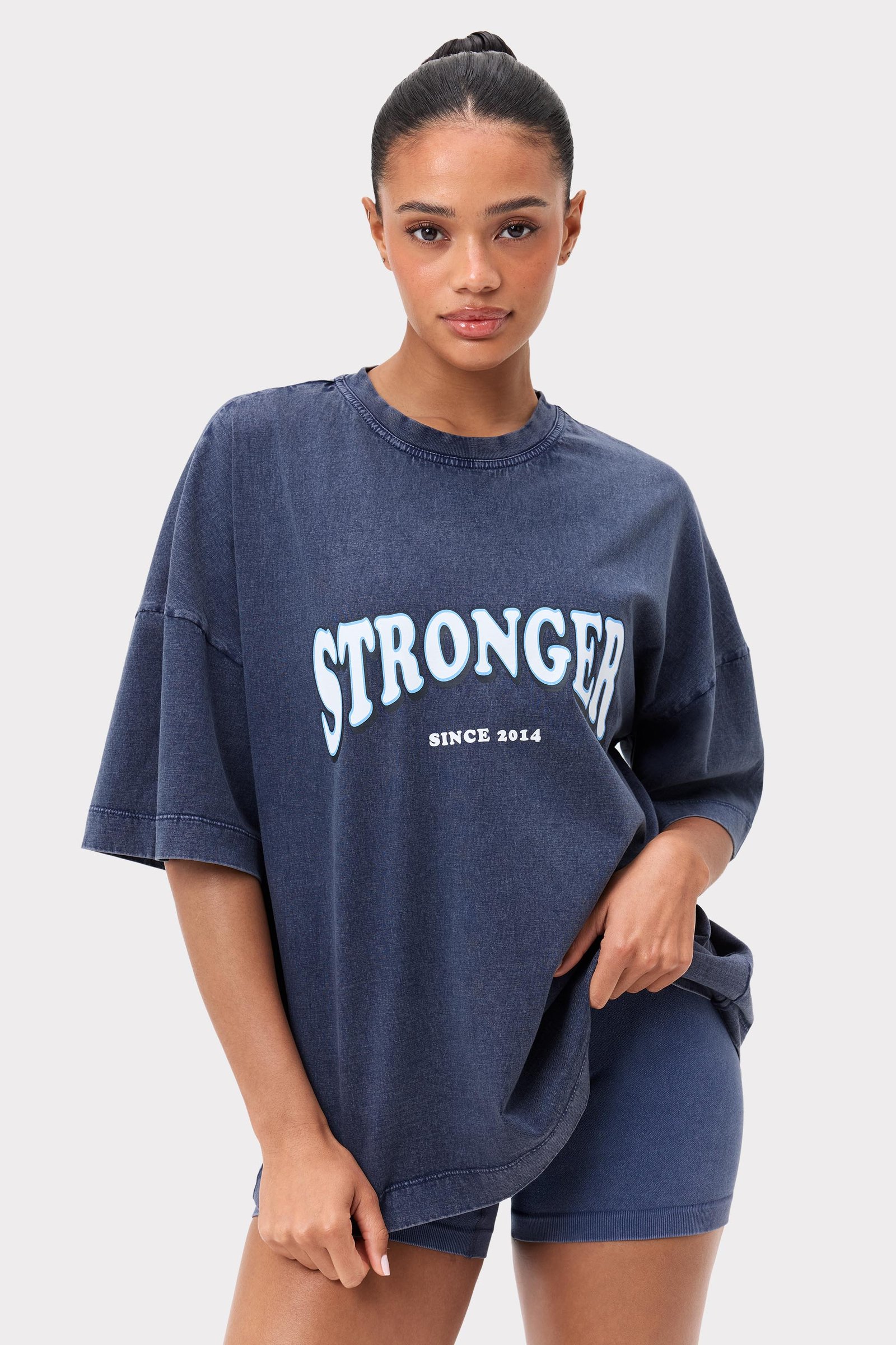 Model in het gewassen marineblauwe Oversized Crew T-shirt van Stronger, een biologisch katoenen top met vintage-stijl logo.