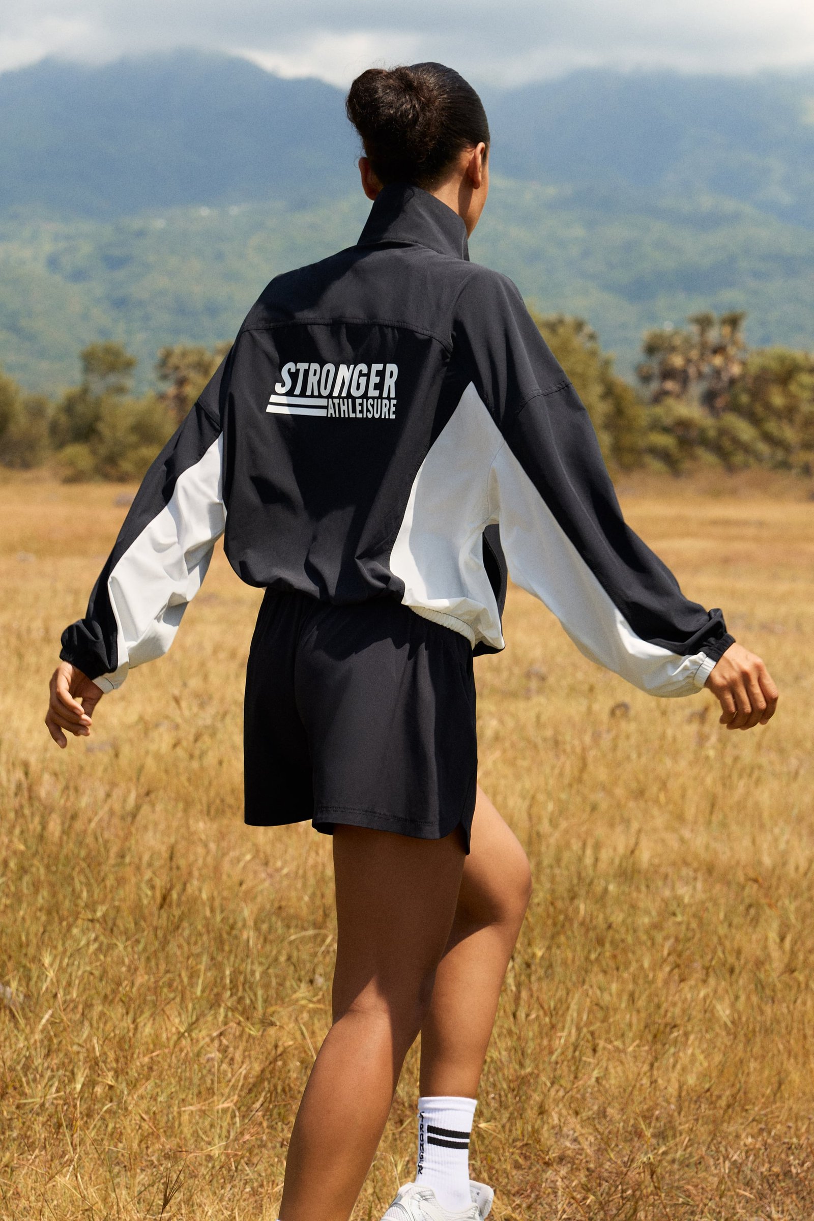 Stronger's black and white Breezy Woven Jacket with a bold back logo and loose fit, seen in an outdoor setting.