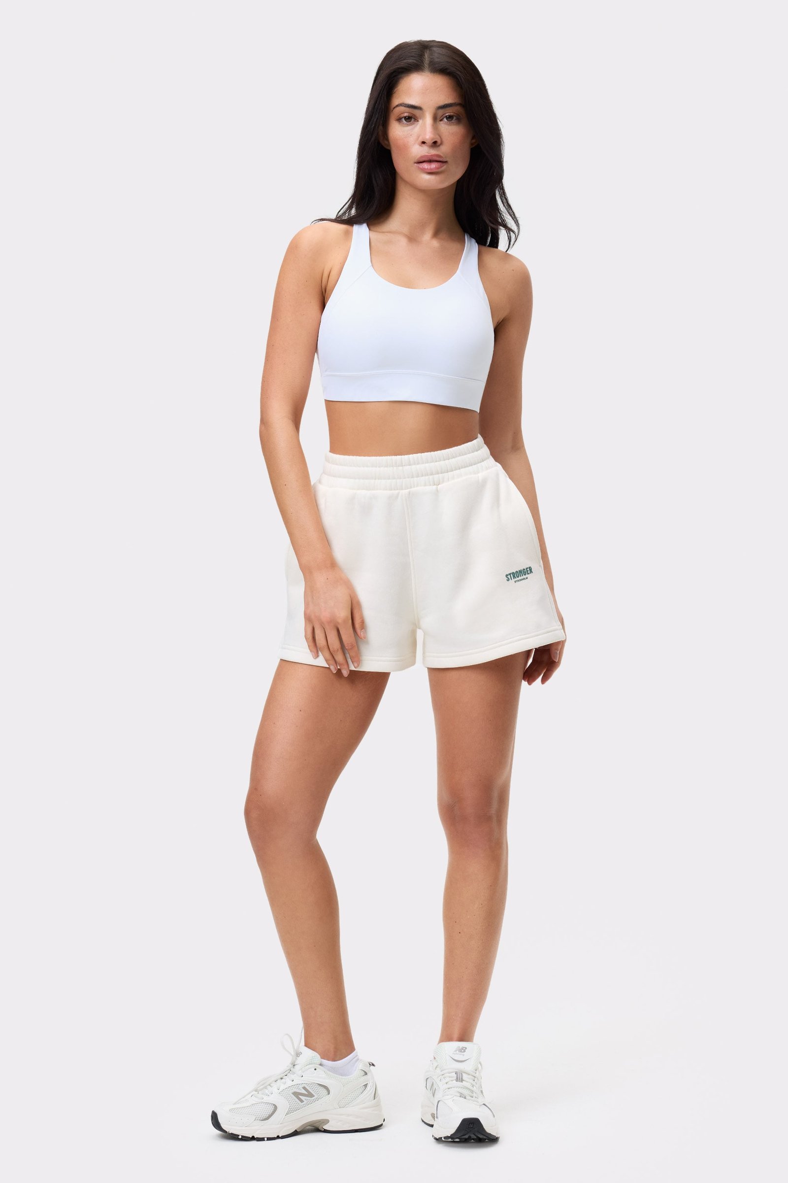 Model trägt die hoch taillierten Comfy Sweatshorts in Whisper White von Stronger, kombiniert mit einem weißen Sport-BH.
