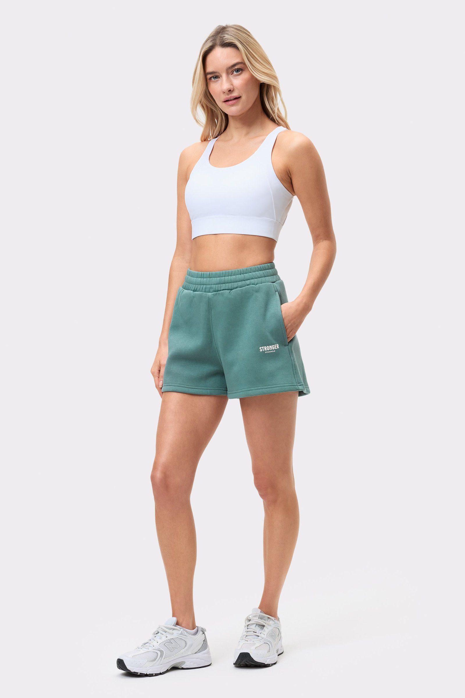 Vorderansicht eines Models, das die grünen Comfy Sweatshorts von Stronger trägt, kombiniert mit einem weißen Sport-BH.