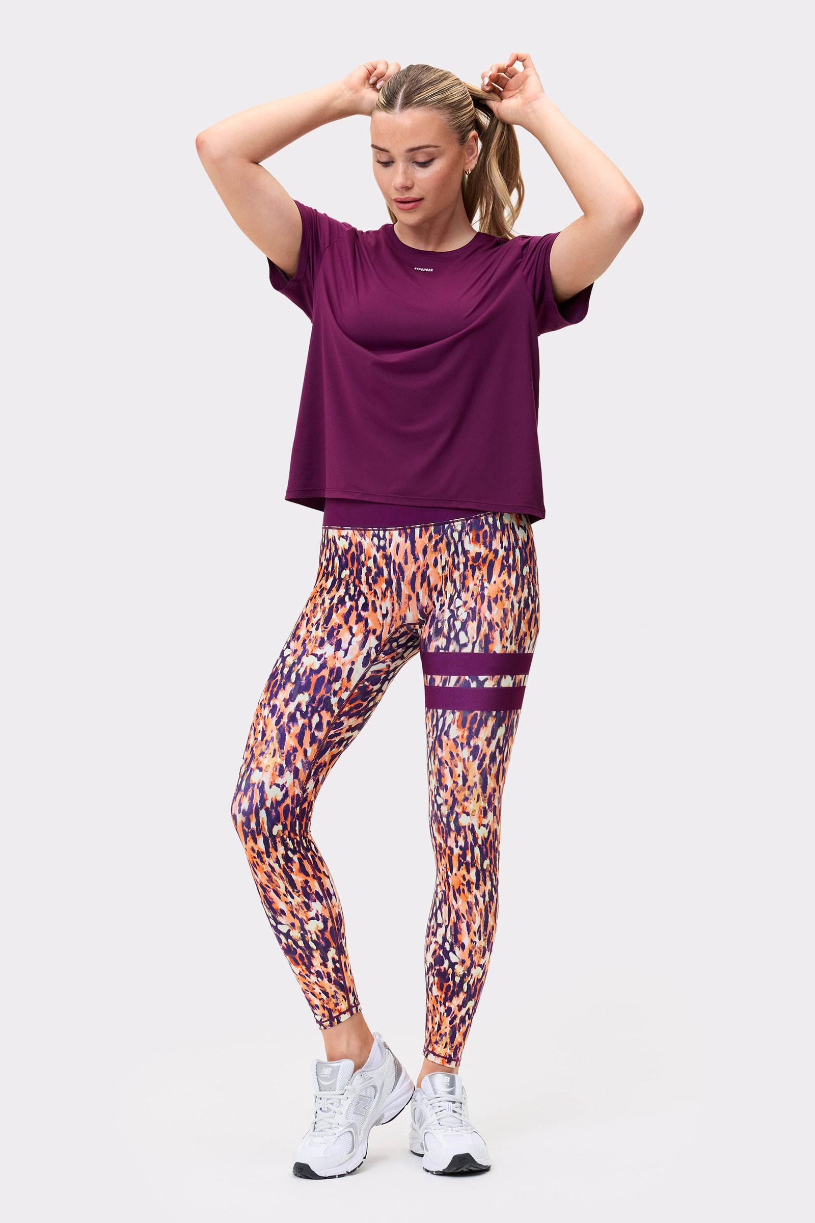 Front view of a model wearing the `Relaxed Tee` in `Aubergine Purple` from `stronger`, paired with patterned leggings.
