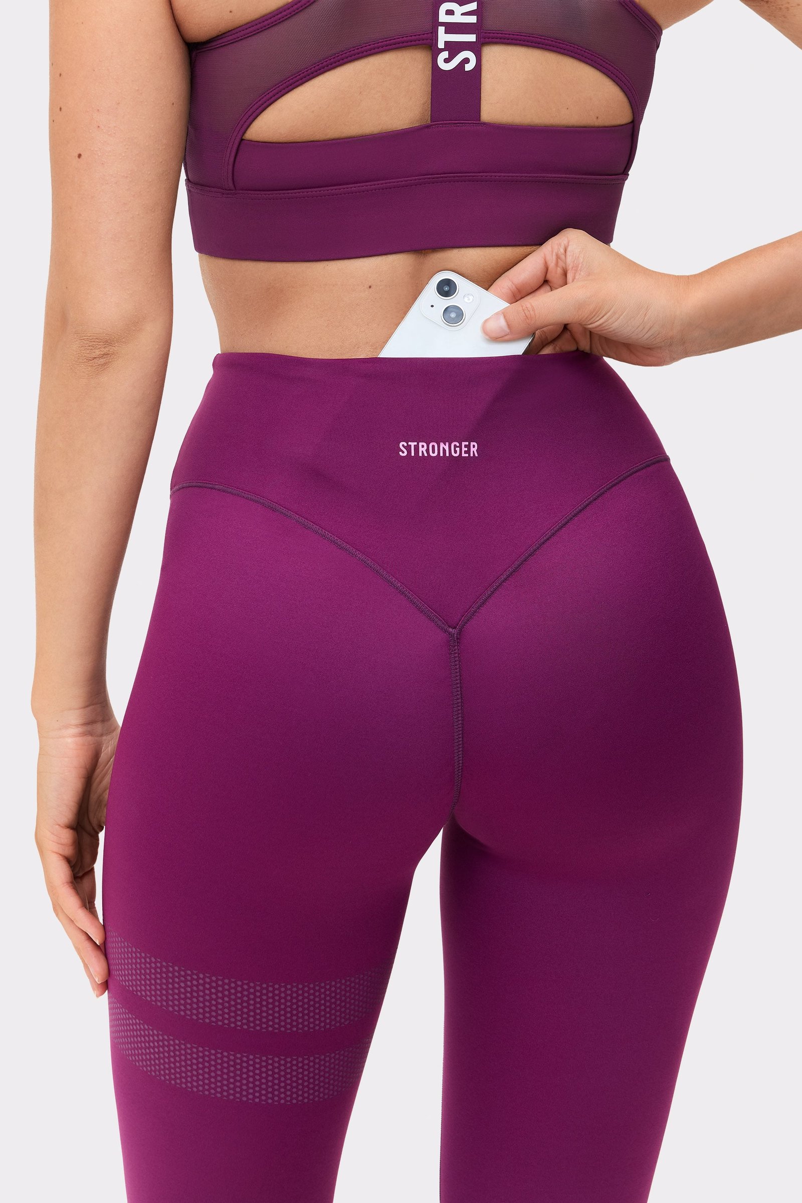 Close-up of a model putting her phone in the back pocket of The Signature One Contour Leggings from stronger.