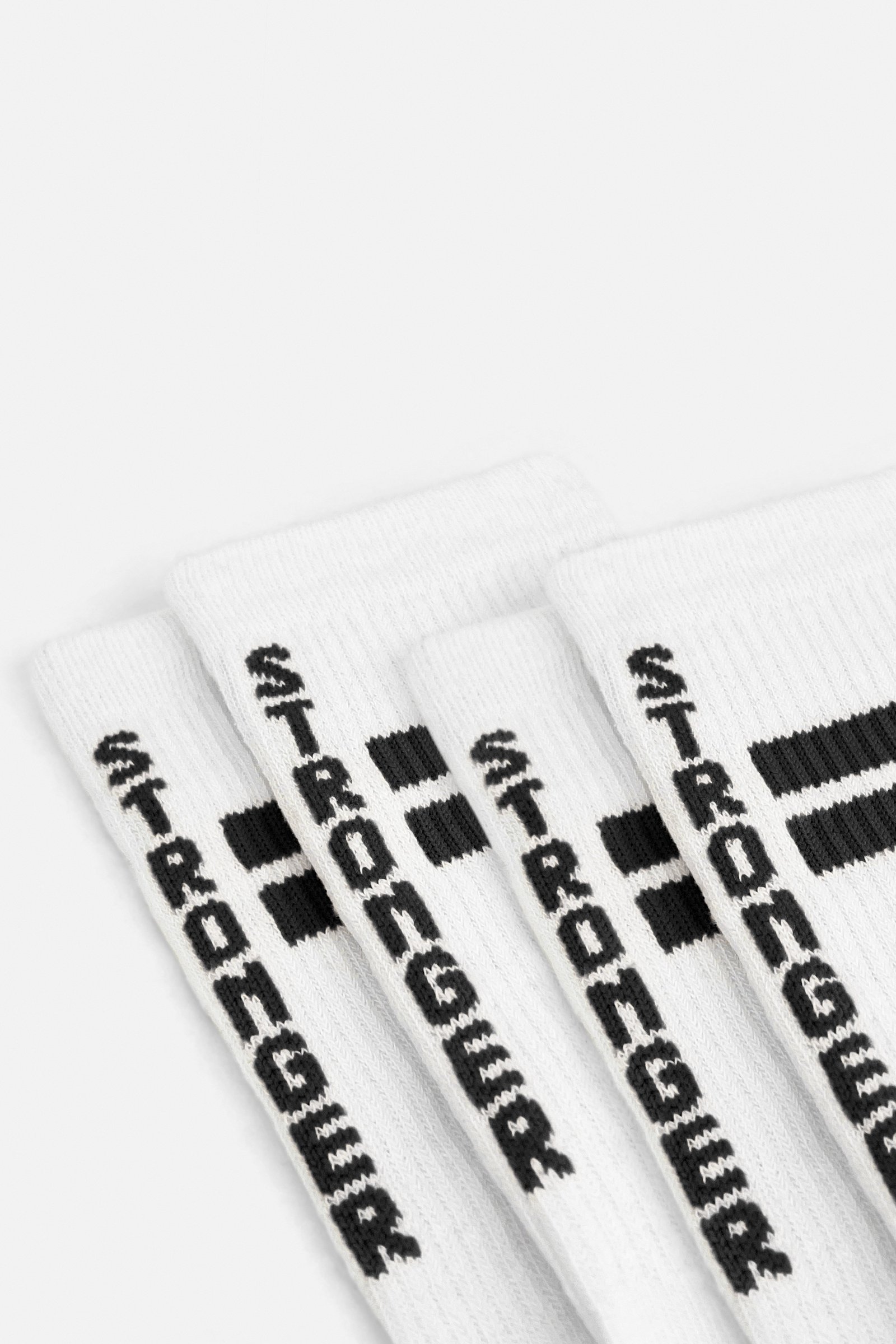 Nahaufnahme der weißen Stride Socks von Stronger mit schwarzen Logodetails und Signature Lines auf geripptem Stoff.