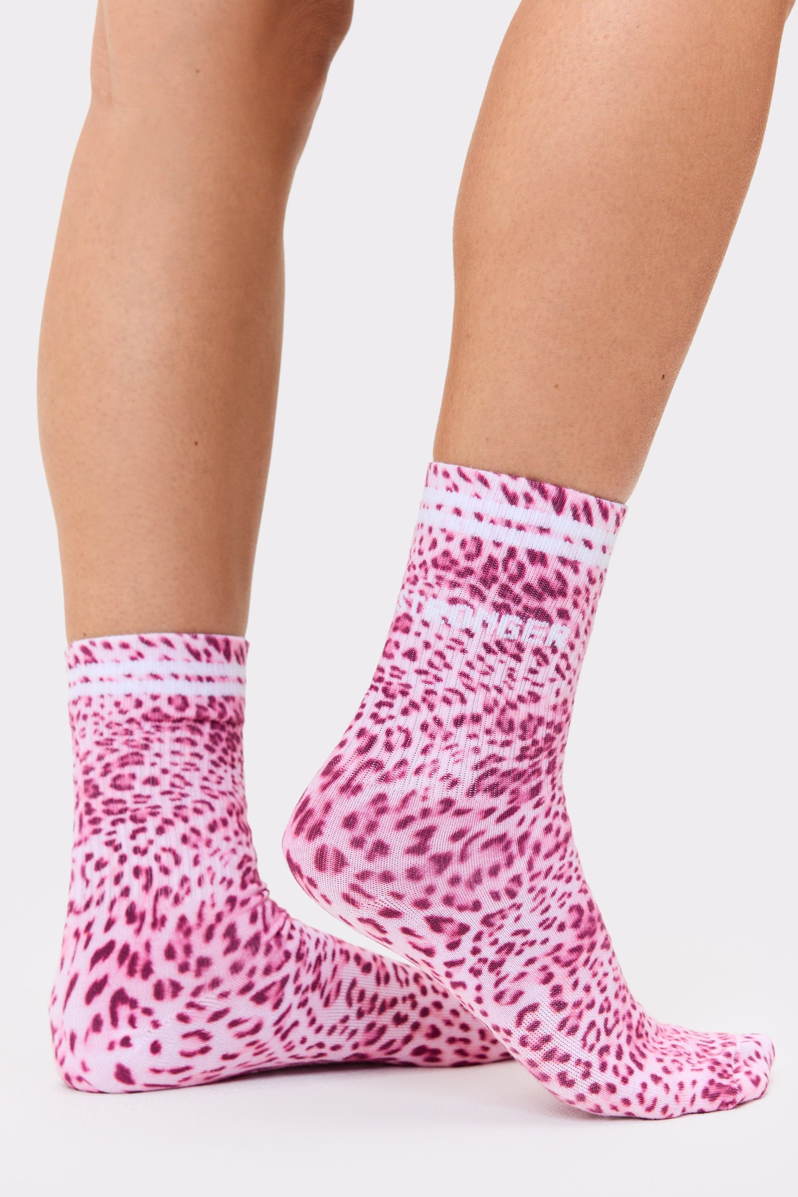 Close-up of a person wearing the pink leopard print Essential Socks from stronger with signature stripes.