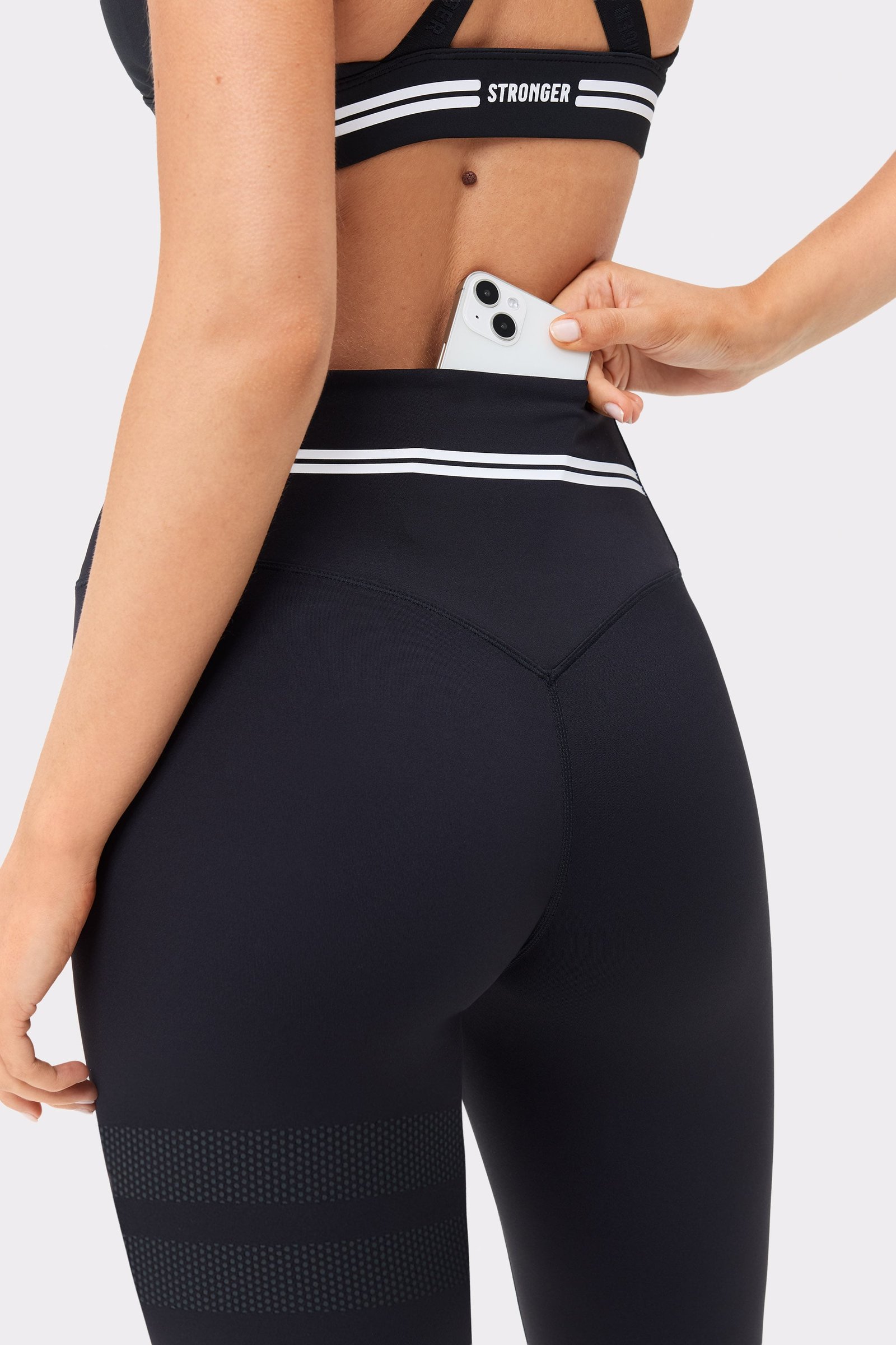 Stronger black Signature Logo Leggings shown from the back, featuring a phone in the waistband pocket and white stripes.