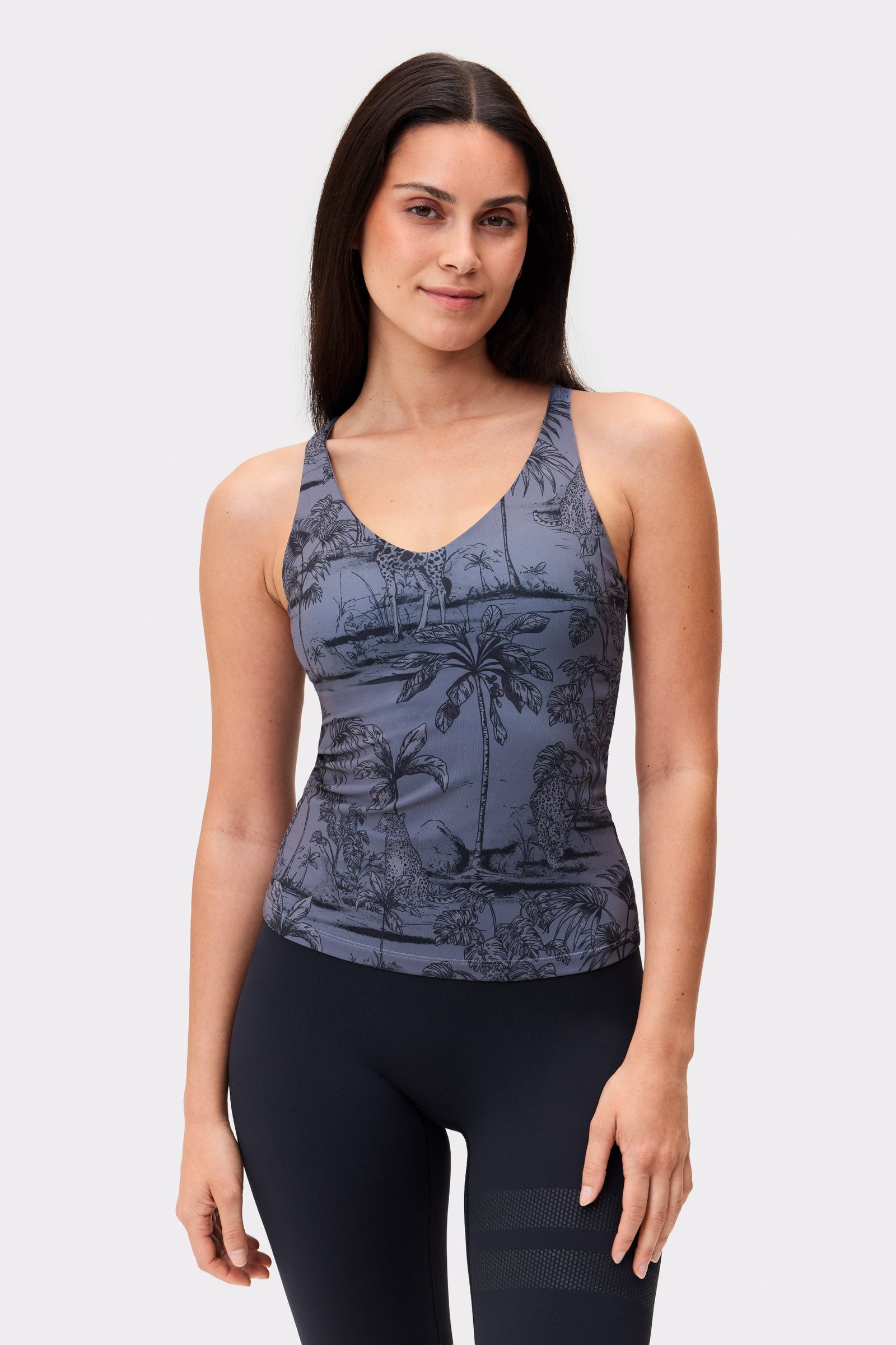 Model trägt das dunkelgraue Signature Strappy Tank von Stronger mit szenischem Toile-Print, designt für aktive Workouts.