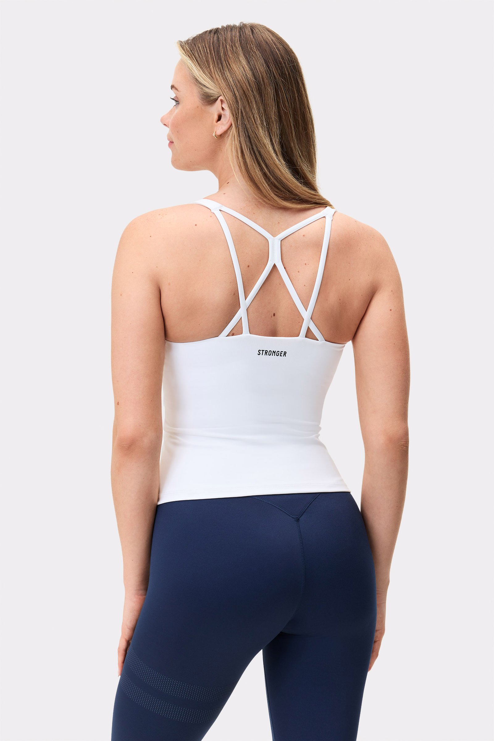 Model im weißen Stronger Signature Strappy Tank, zeigt das schmale Rückendesign mit Trägern und dem Logo.