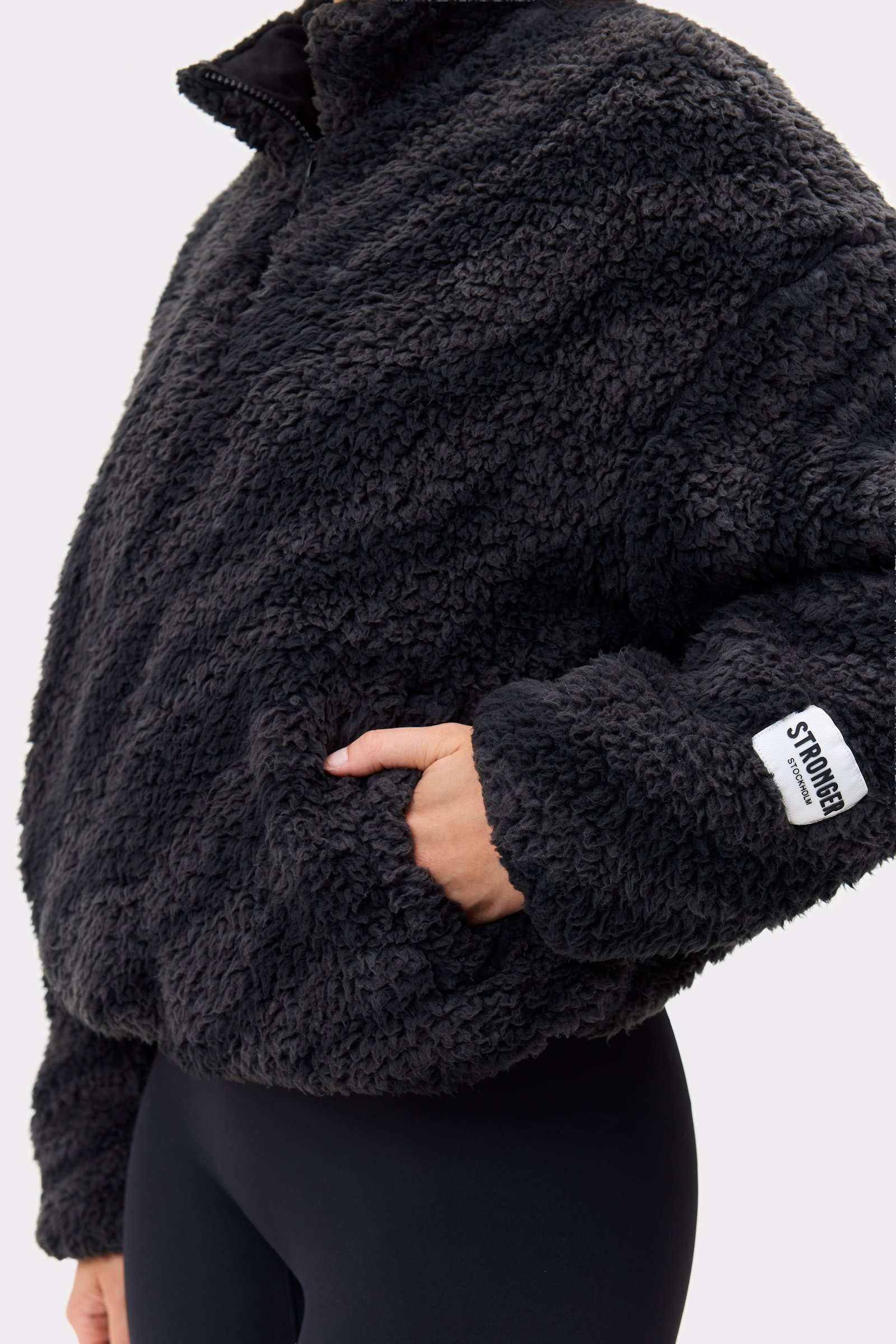 Nahaufnahme der schwarzen Pile Half Zip Jacket von Stronger mit kuscheliger Teddy-Textur und Ärmellogo.