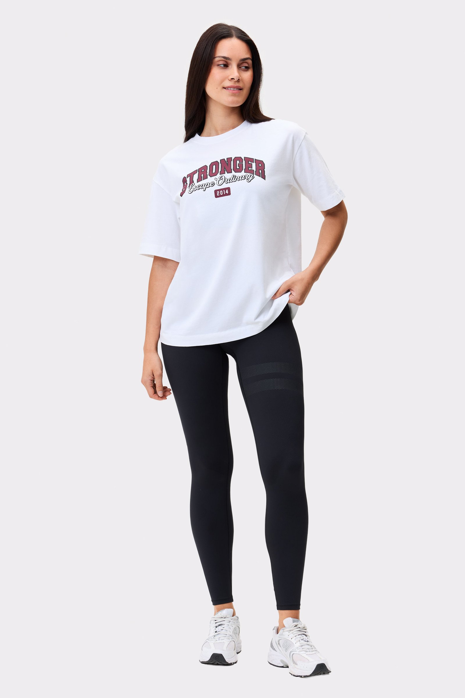 Model trägt das hellweiße Essential T-Shirt von Stronger mit einem Frontprint und schwarzen Leggings.