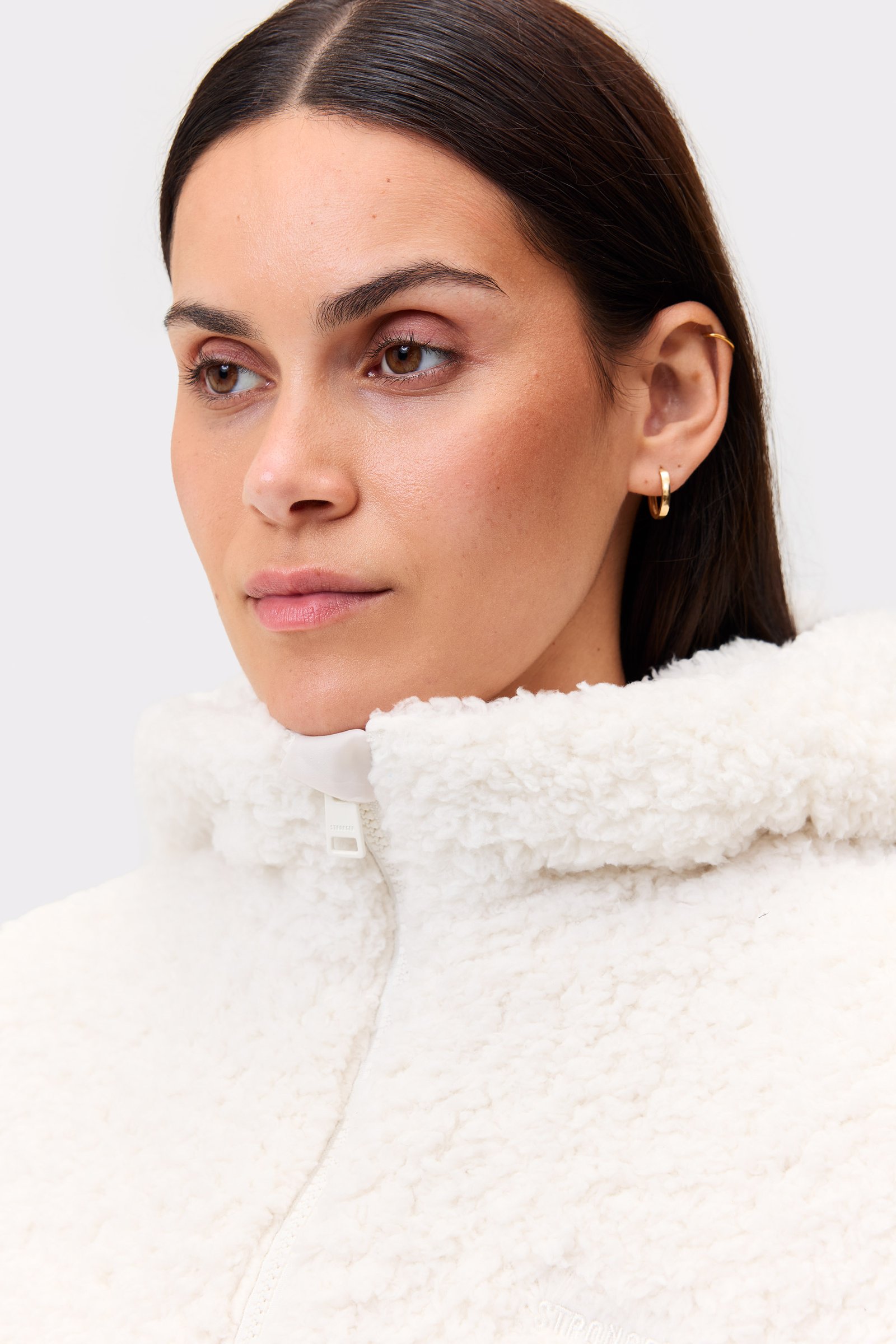 Nahaufnahme eines Models in der weichen, weißen Hooded Pile Jacket von Stronger mit kuscheliger Fleece-Textur.