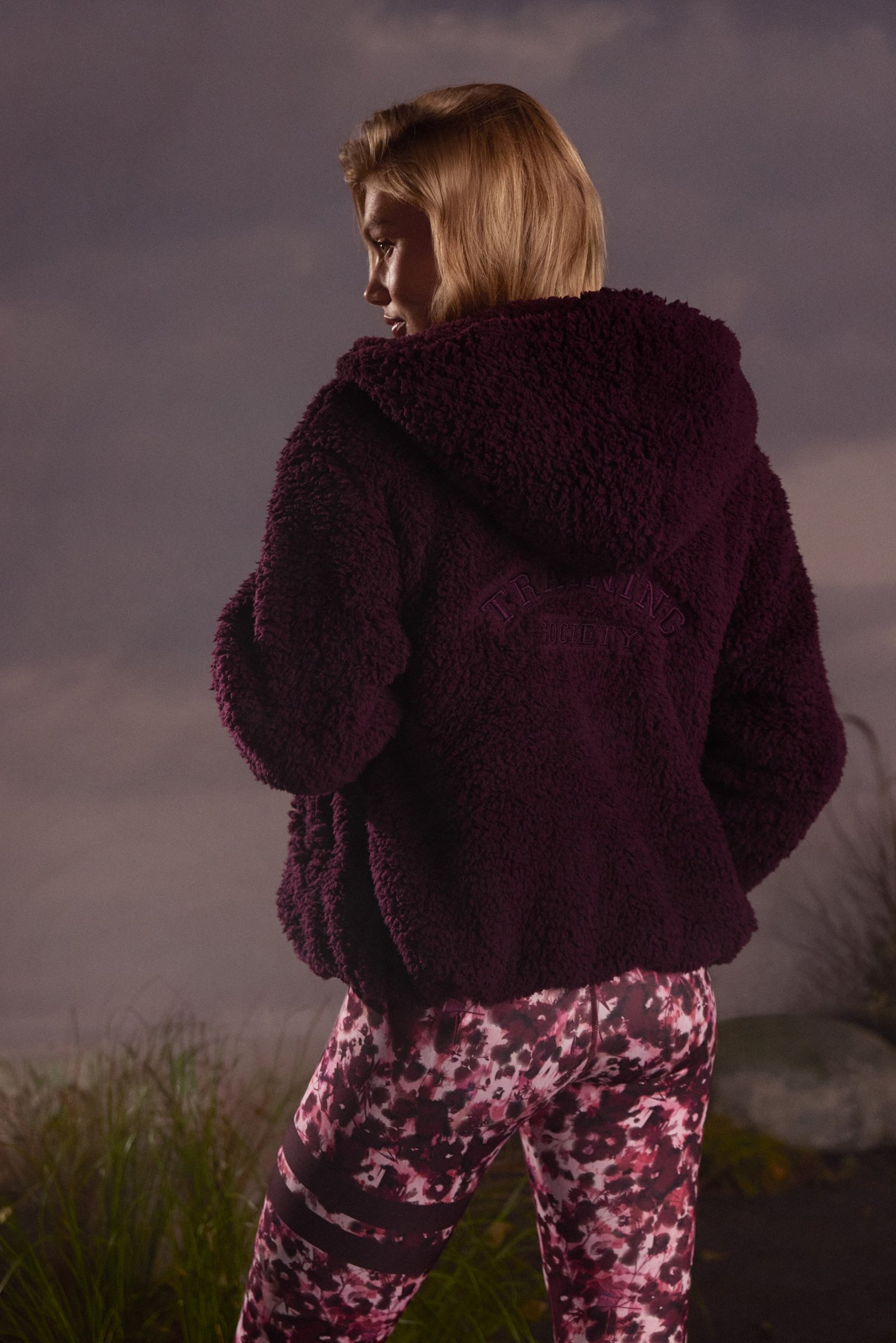 Back view of a woman wearing the dark purple Hooded Pile Jacket from Stronger, showing the soft pile texture.