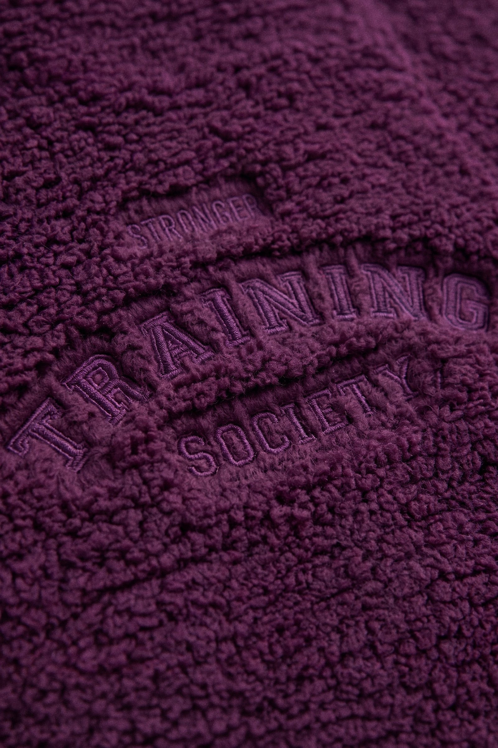 Close-up of embroidered back detail on the dark purple Hooded Pile Jacket from stronger, showcasing the soft texture.