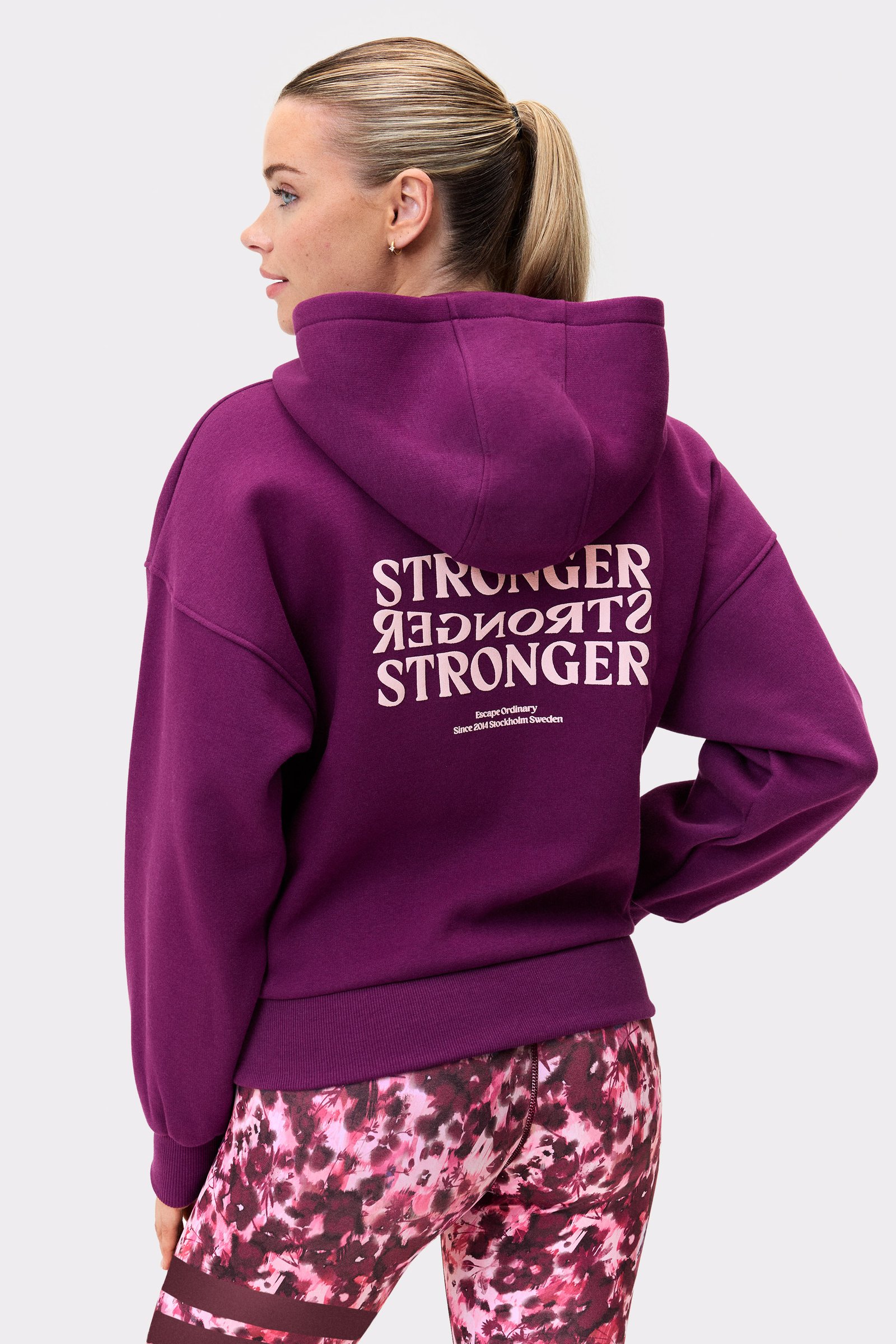 Back view of a person wearing the stronger Relaxed Full Zip Hoodie in aubergine purple, showing the center-back graphic.