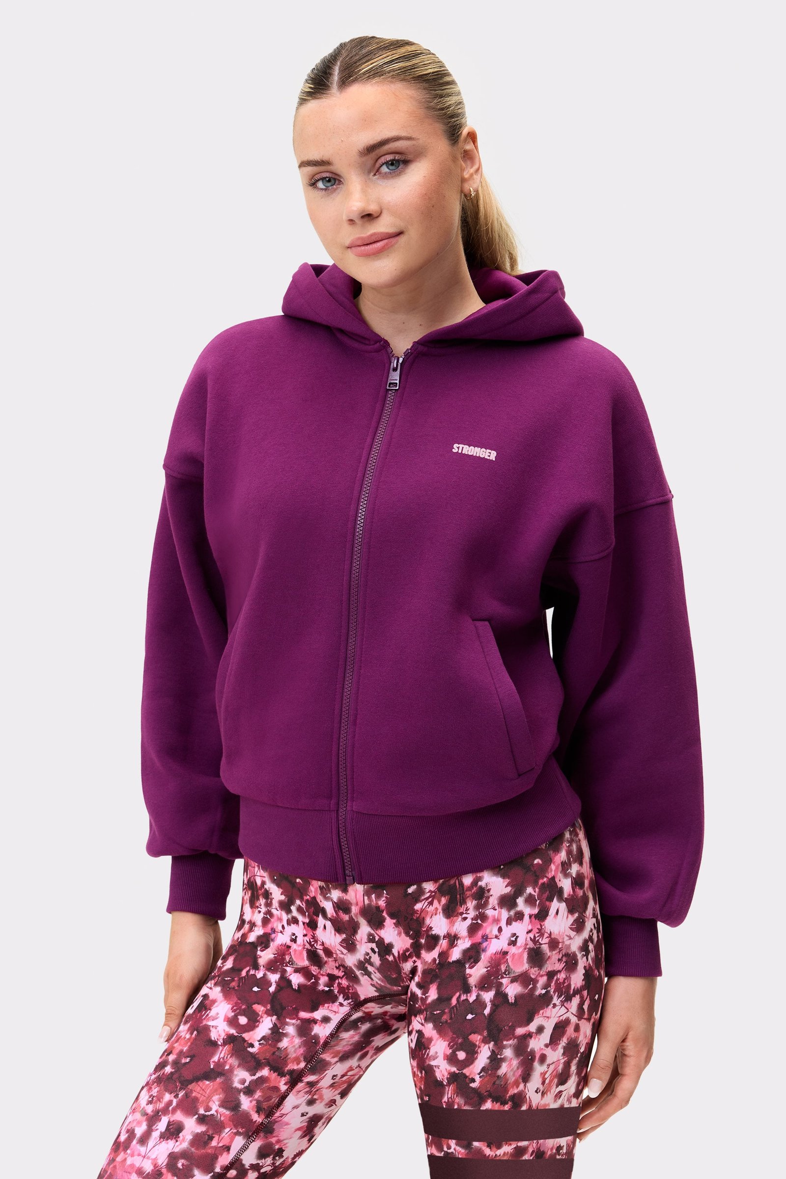Front view of a model in the aubergine purple Relaxed Full Zip Hoodie from stronger, showing the front zip and chest logo.